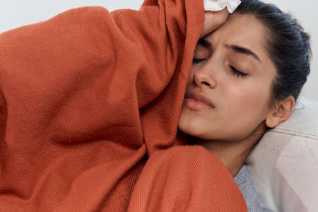 woman lies at home on the couch covered with a blanket with closed eyes cold
