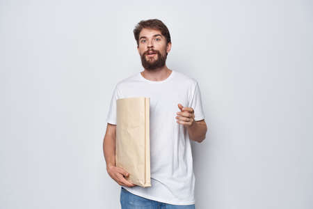 a man in a white T-shirt with a paper bag in his hands on a light backgroundの写真素材