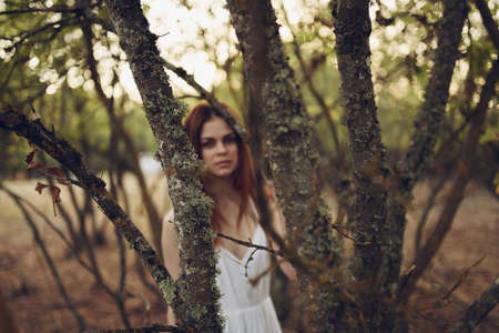 pretty woman in white dress near trees fallen leaves in the forestの写真素材