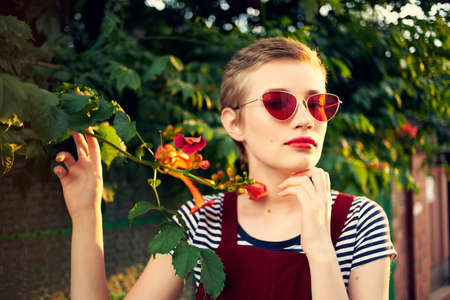 woman in sunglasses stands next to a bush of flowers in the street lifestyleの写真素材