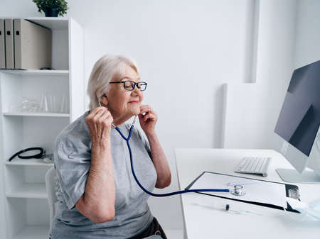elderly woman sitting at the table stethoscope vaccine passport treatment diagnosisの写真素材
