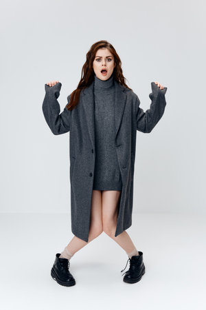 a woman in a gray sweater and a coat is dancing on a light background and black shoesの写真素材