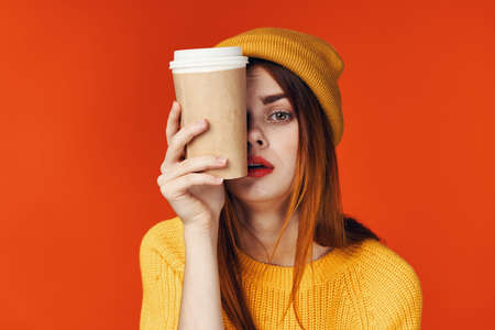 red-haired woman in a hat wearing a sweater with a cup of coffee lifestyle red backgroundの写真素材