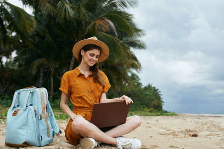 woman on the island sits on the sand in front of a laptop remote workの写真素材