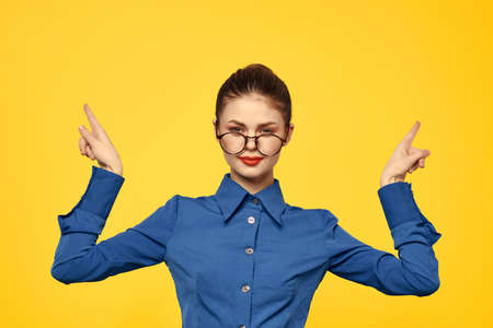 woman in a blue shirt with glasses gesturing with her hands yellow background posingの写真素材