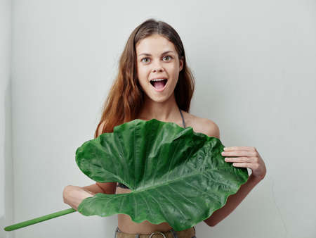 emotional woman with open mouth hides behind green leaf light backgroundの写真素材