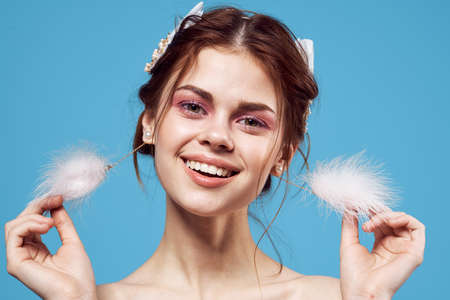 attractive woman naked shoulders fluffy earrings cosmetics blue background