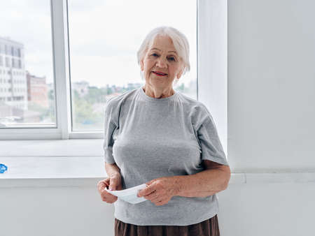 elderly woman with a medical mask in her hands near the window medicineの写真素材