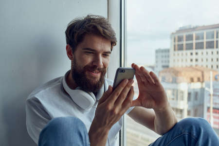 bearded man sitting near the window in headphones listening to music on headphonesの写真素材