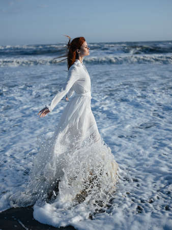 Woman in white dress walking along the coast of the ocean Freedom fashionの写真素材