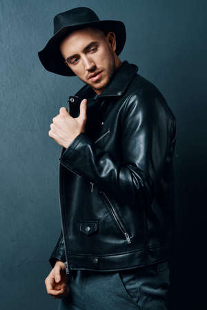 Cheerful fashionable man in leather jacket posing against dark background