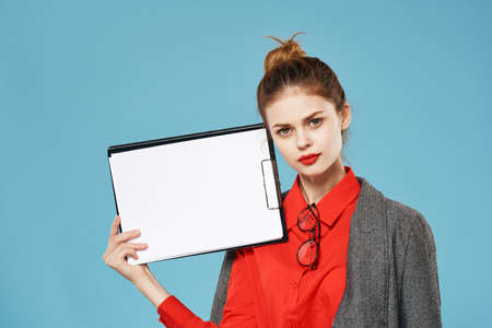 woman in a red shirt with a jacket holds a sheet of paper Copy Space blue background
