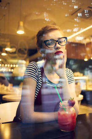 woman with glasses sitting at a table in a cafe with a cocktail drink leisure lifestyleの写真素材