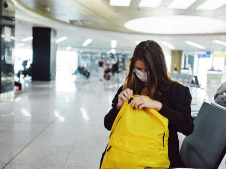 woman in medical mask hits airport yellow backpack waitingの写真素材