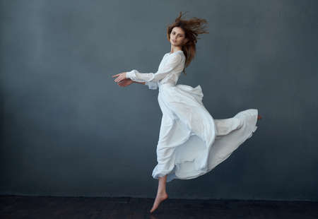 pretty woman dancing in white dress studio isolated background fashionの写真素材