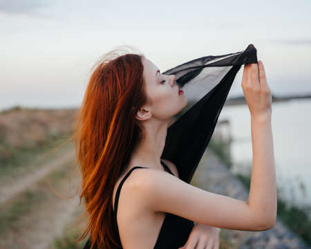pretty red-haired woman in black dress outdoors posing fresh airの写真素材