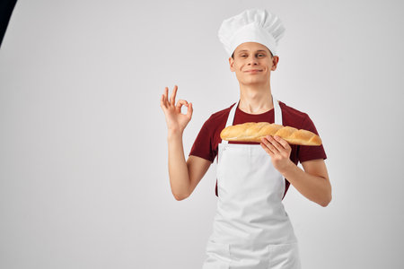 Baker in a white apron loaf in the hands of cookingの写真素材