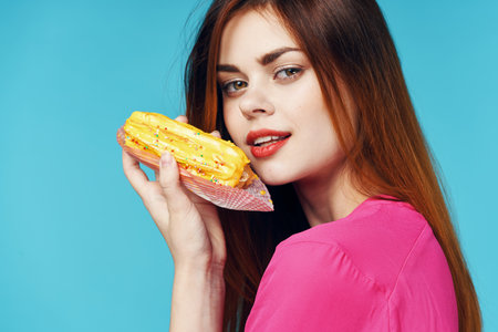 woman in a pink sweater with an eclair in her hands near her face close-up Glamor