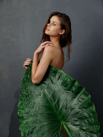 charming woman with green leaf covers naked body dark backgroundの写真素材