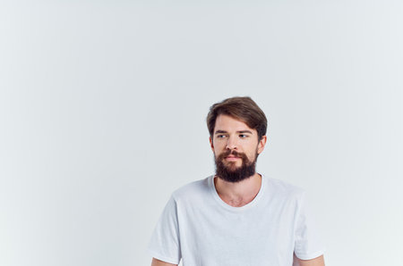 bearded man in white t-shirt sits on a chair light backgroundの写真素材