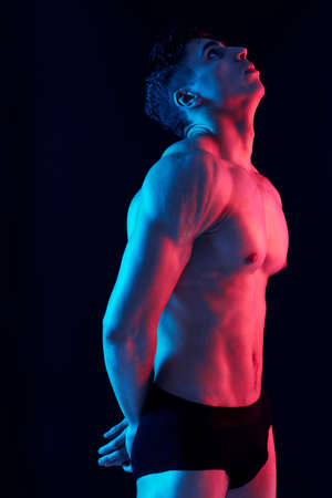 sexy man with a pumped-up torso posing on a dark background side viewの写真素材