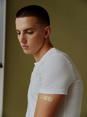 a man in a white t-shirt with an adhesive plaster on his shoulder immunity covid19 passportの写真素材
