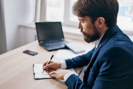 bearded man sitting at a desk in front of a laptop finance officialの写真素材