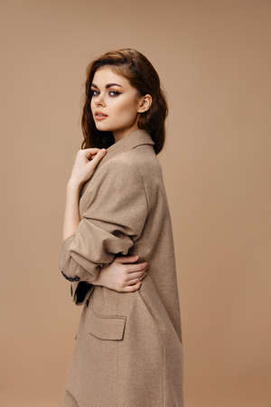 woman in coat hugs herself with hands on beige background hairstyle makeup modelの写真素材