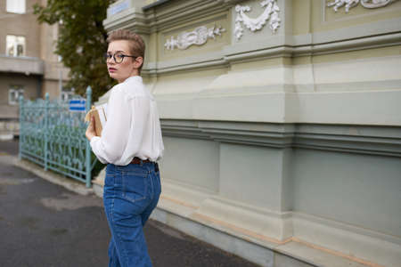 short haired woman with glasses walking around the city with a book educationの写真素材