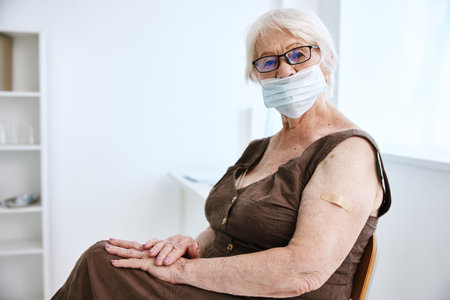 elderly woman wearing glasses with plaster on her hand covid passport hospitalの写真素材