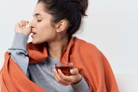 woman hiding with a plaid at home with a cup of tea treating infectionの写真素材