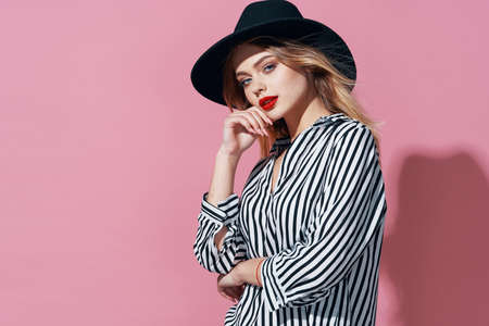 glamorous woman in black hat and striped shirt bright makeup pink background