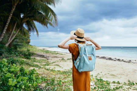 woman in a sundress and hat on the island near the trees and the sea Backpack in the backgroundの写真素材