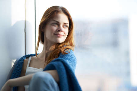 beautiful woman sitting on the windowsill with a blue plaidの写真素材