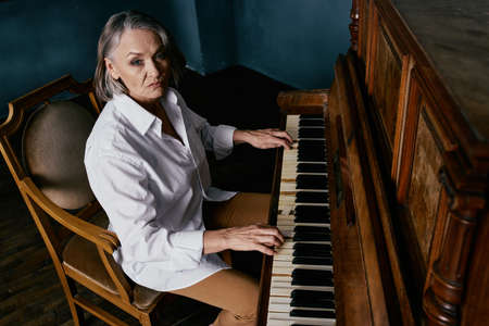 a woman in a white shirt sits on a chair next to a piano learning musicの写真素材