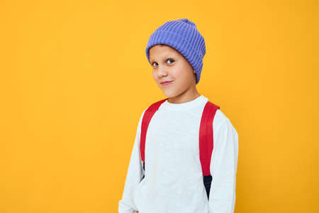 boy wearing blue hat school backpack posing yellow backgroundの写真素材