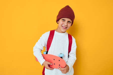 happy schoolboy in a red hat skateboard in his hands yellow color backgroundの写真素材