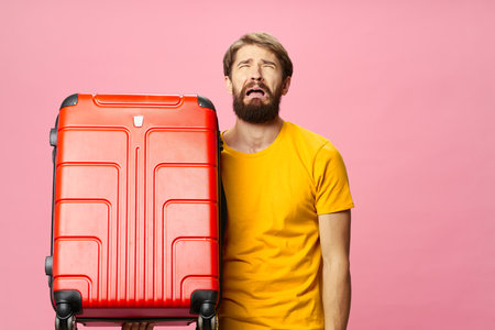 man in yellow t-shirt with red suitcase on pink background travel tourismの写真素材