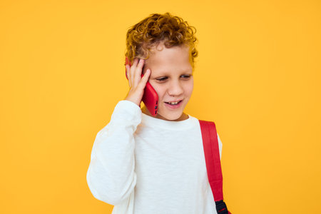 Cheerful young boy in white sweatshirt mobile cell phone red backpack isolated backgroundの写真素材