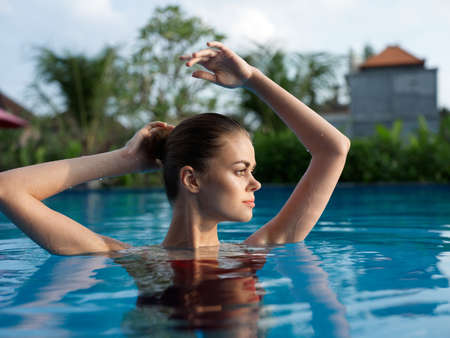 beautiful woman swims in the pool with hands raised up in nature