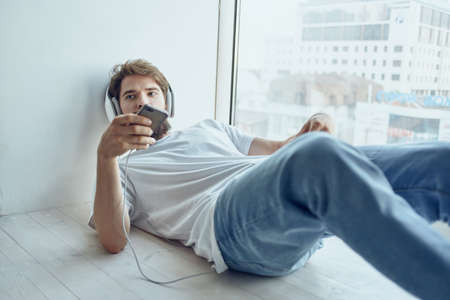 man in white t-shirt lying on the windowsill wearing headphones technologyの写真素材