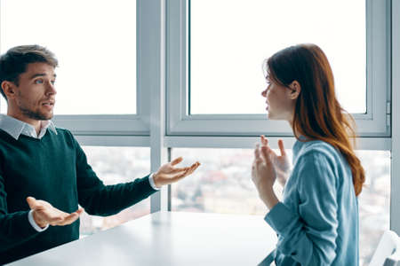 surprised man sits at a table and gestures with his hands and an interested woman
