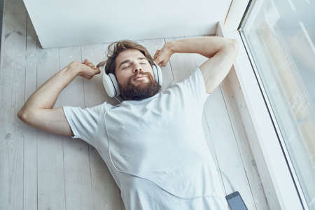 young man lying near the window wearing headphones hipster