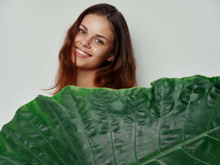 green leaf of palm tree in front of a woman with red hair on a light background clean skin model