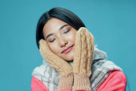 woman in mittens touches her face with her hands and a warm scarf Pink sweater asian appearance modelの写真素材