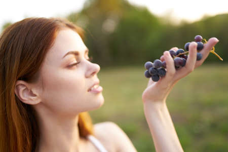 cheerful pretty woman outdoors eating grapes fresh airの写真素材