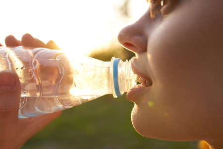 woman outdoors drinking water from a bottle of refreshmentの写真素材