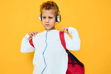 portrait of a boy with a red backpack wearing headphones yellow backgroundの写真素材