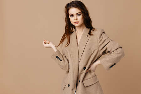 sexy woman in a coat on a beige background gestures with her handsの写真素材
