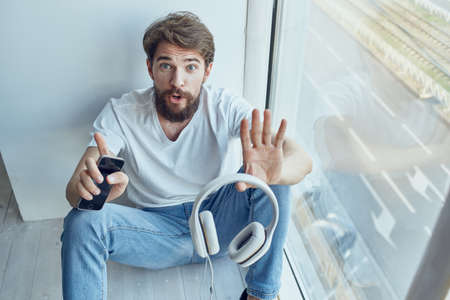 Man sitting on the windowsill in headphones in headphones technologyの写真素材